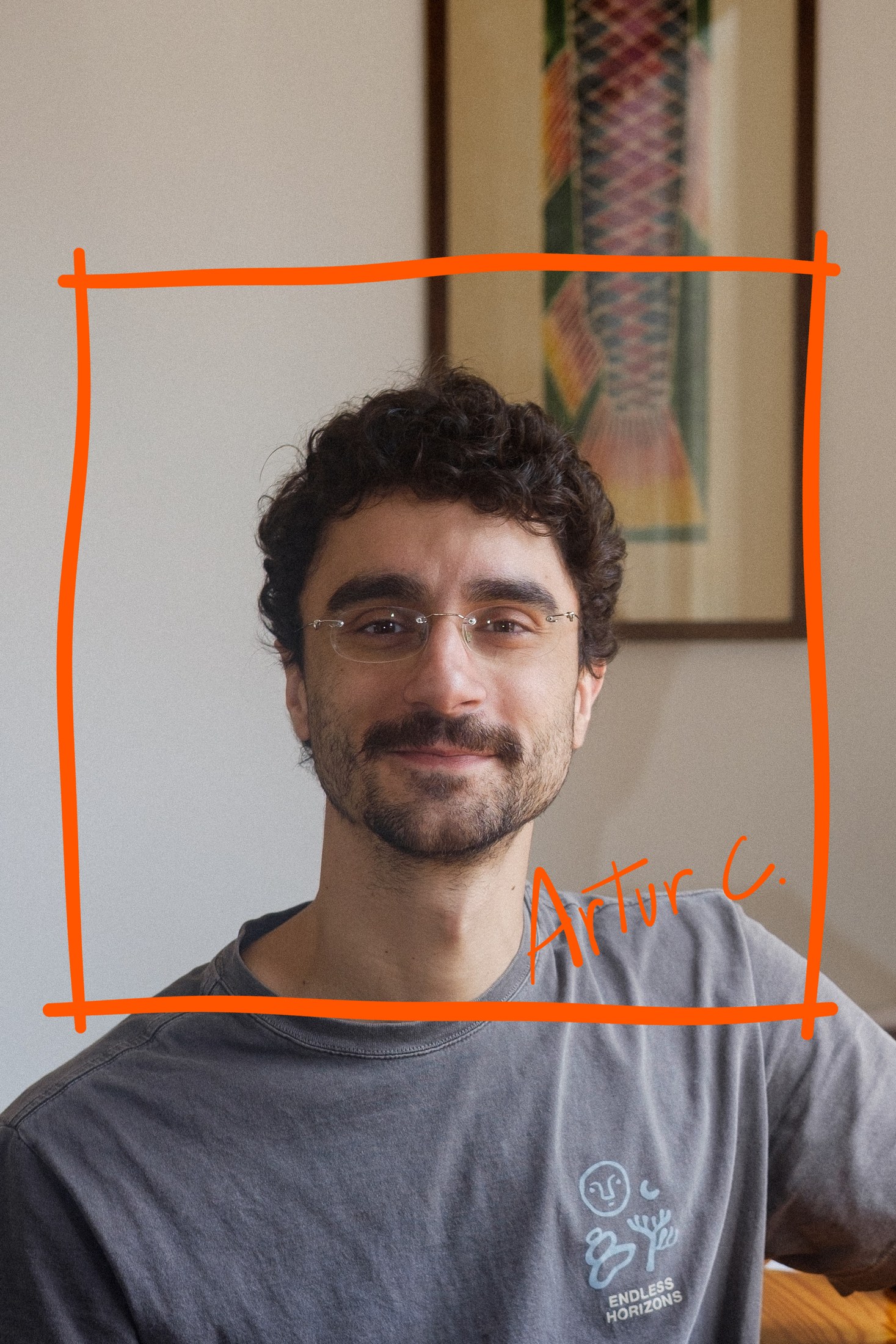 Artur, de óculos finos e cabelo cacheado, sorrindo para a câmera, de camiseta cinza, diante de um quadro com um peixe. Um quadrado laranja riscado à mão o envolve e a assinatura “Artur C.” aparece inclinada na quina de baixo.
