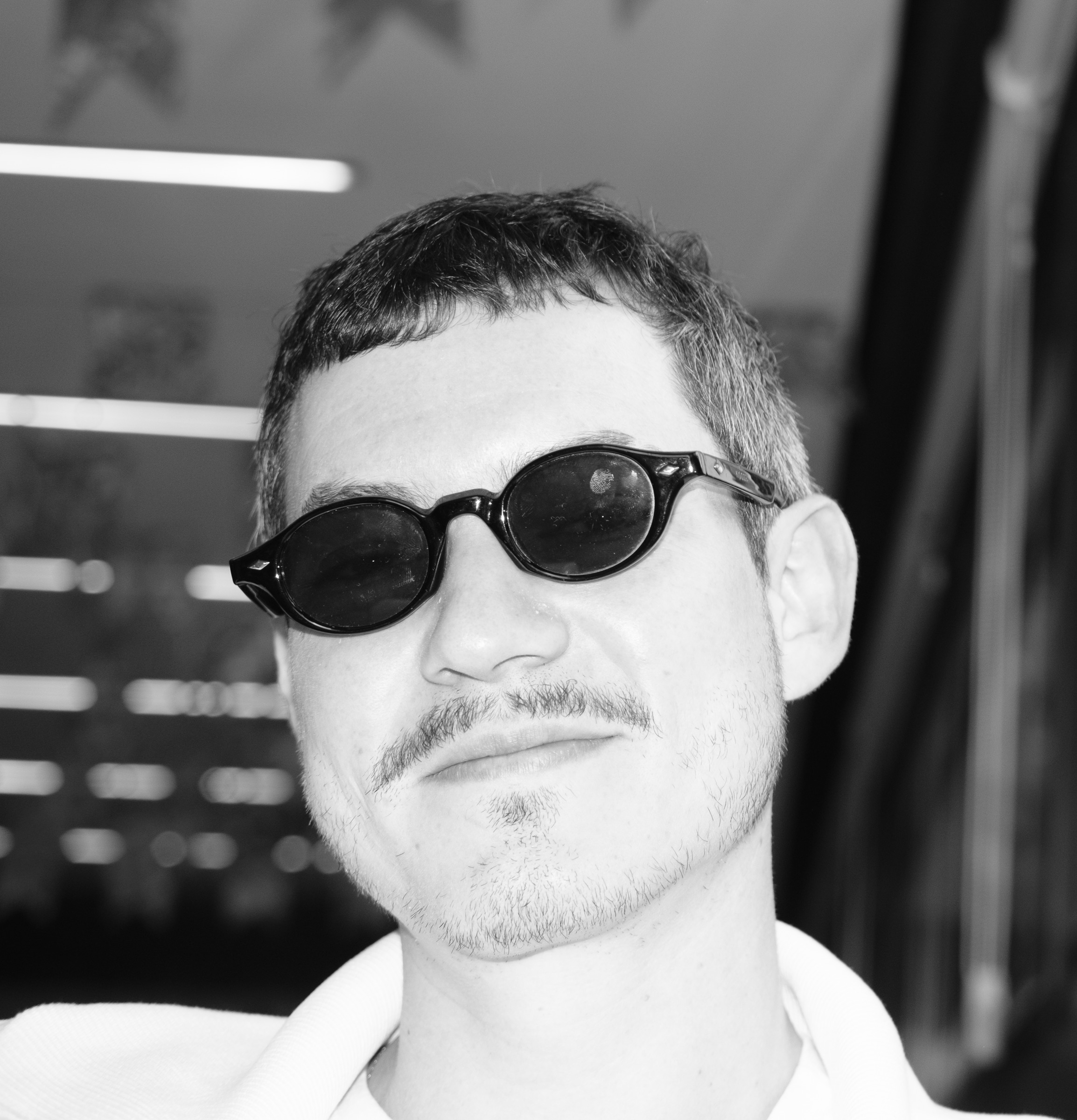 Close de Felipi em preto e branco, de óculos escuros e bigode, olhando para a câmera