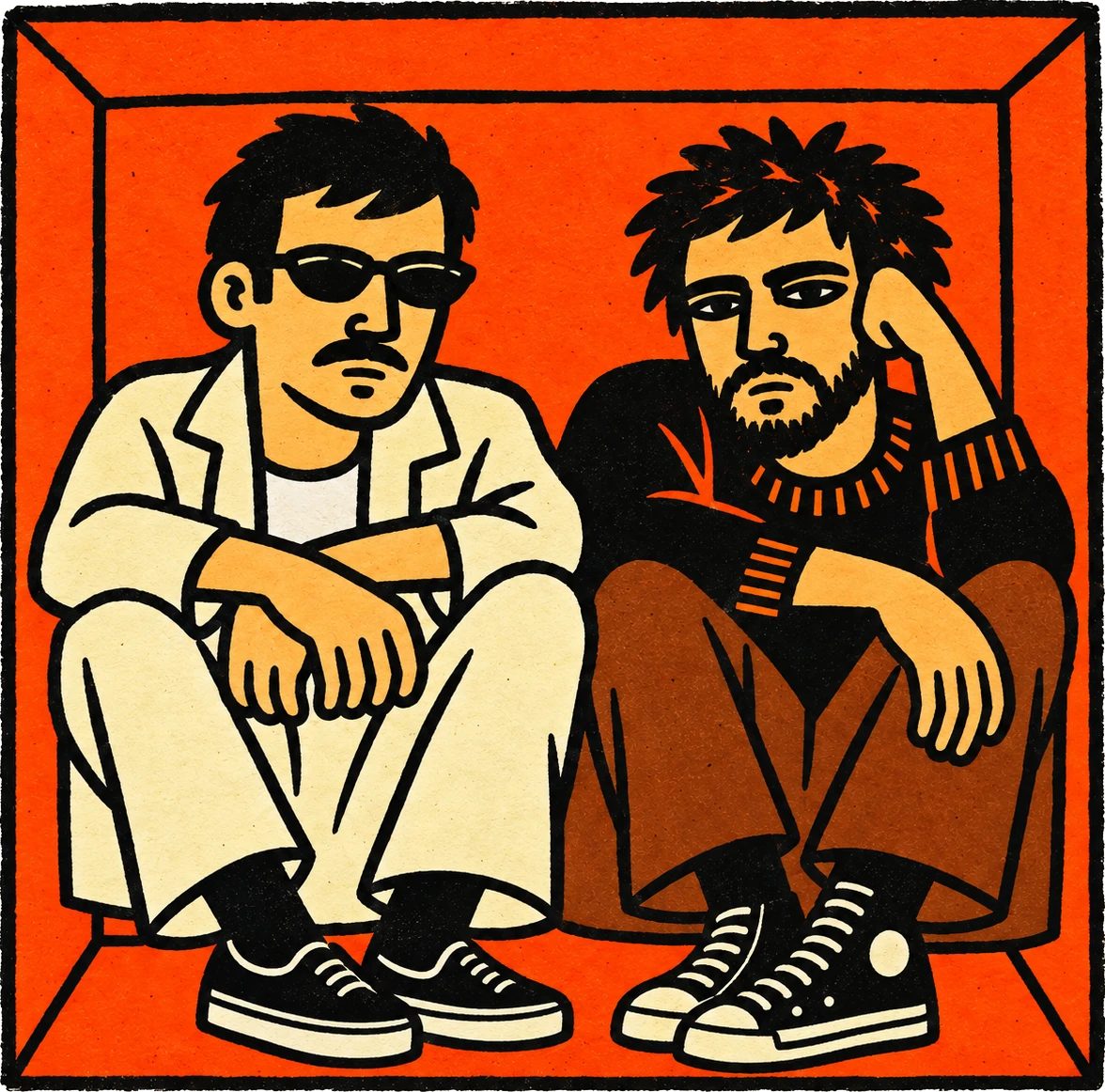Os dois sentados lado a lado dentro de uma caixa laranja: um de óculos escuros e jaqueta creme, o outro de barba e suéter preto