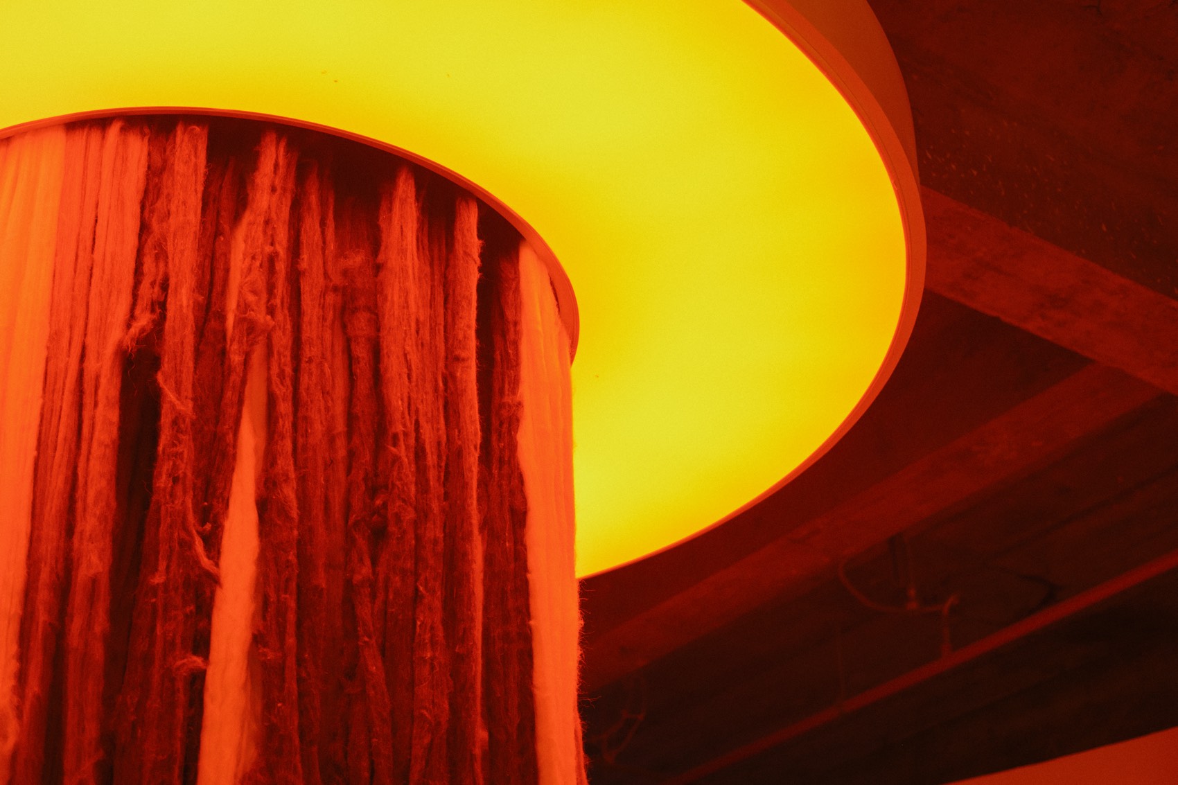 O anel de luz amarelo no teto da exposição, com a cascata de fios de lã caindo por dentro dele