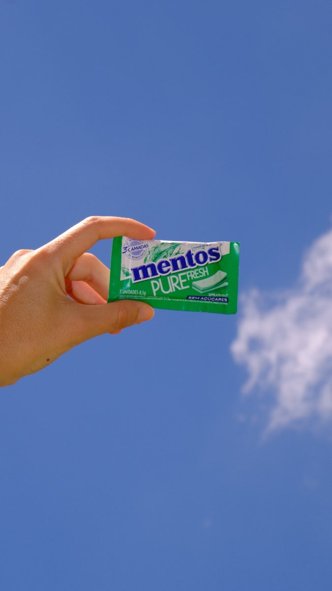Pacote de Mentos erguido contra o céu azul, com uma nuvem ao lado