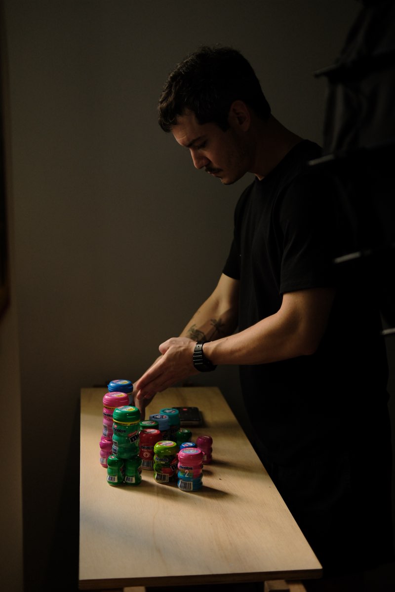 Bastidor: mãos montando uma pilha de potes de Mentos sob luz dura