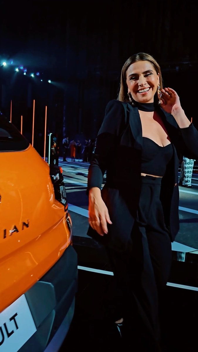 Convidada de preto ao lado do carro laranja, na noite do evento