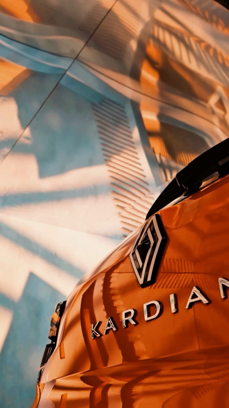 O losango da Renault em relevo no capô laranja de um carro, num facho de luz