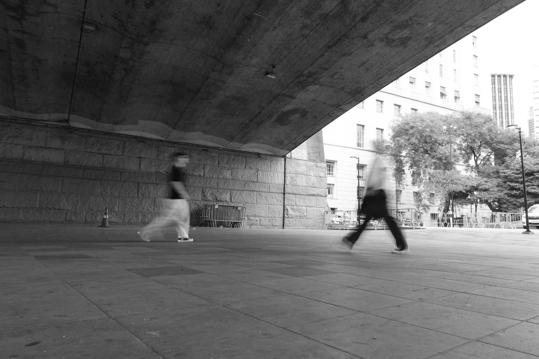 Pedestres atravessando em movimento o vão sob o viaduto, no centro de São Paulo
